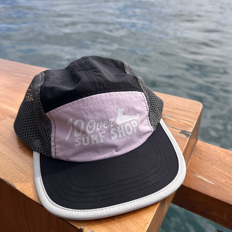 Black cap with pink logo on a wooden surface by water