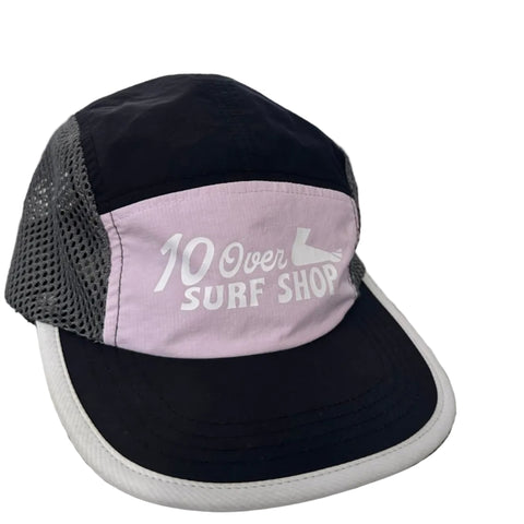 Black and pink cap with '10 Over Surf Shop' logo on a textured surface with a blurred outdoor background.
